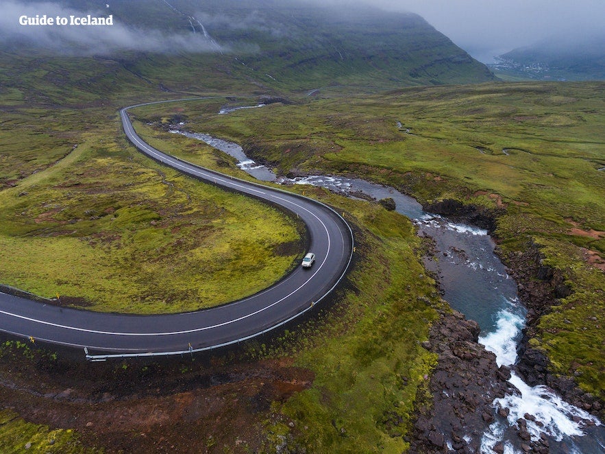 Overhead view of a car driving along the picturesque roads of Iceland, surrounded by greenery and a stream beside the road.