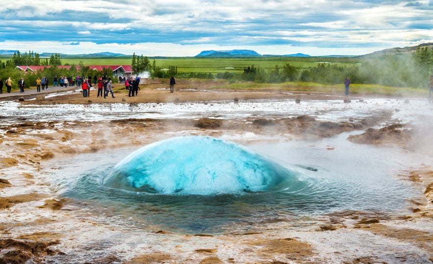 Strokkur geyser about to erupt in Iceland's Golden Circle, with tourists watching the bubbling geothermal activity in summer.
