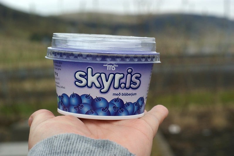 A hand holding a small tub of blueberry skyr.