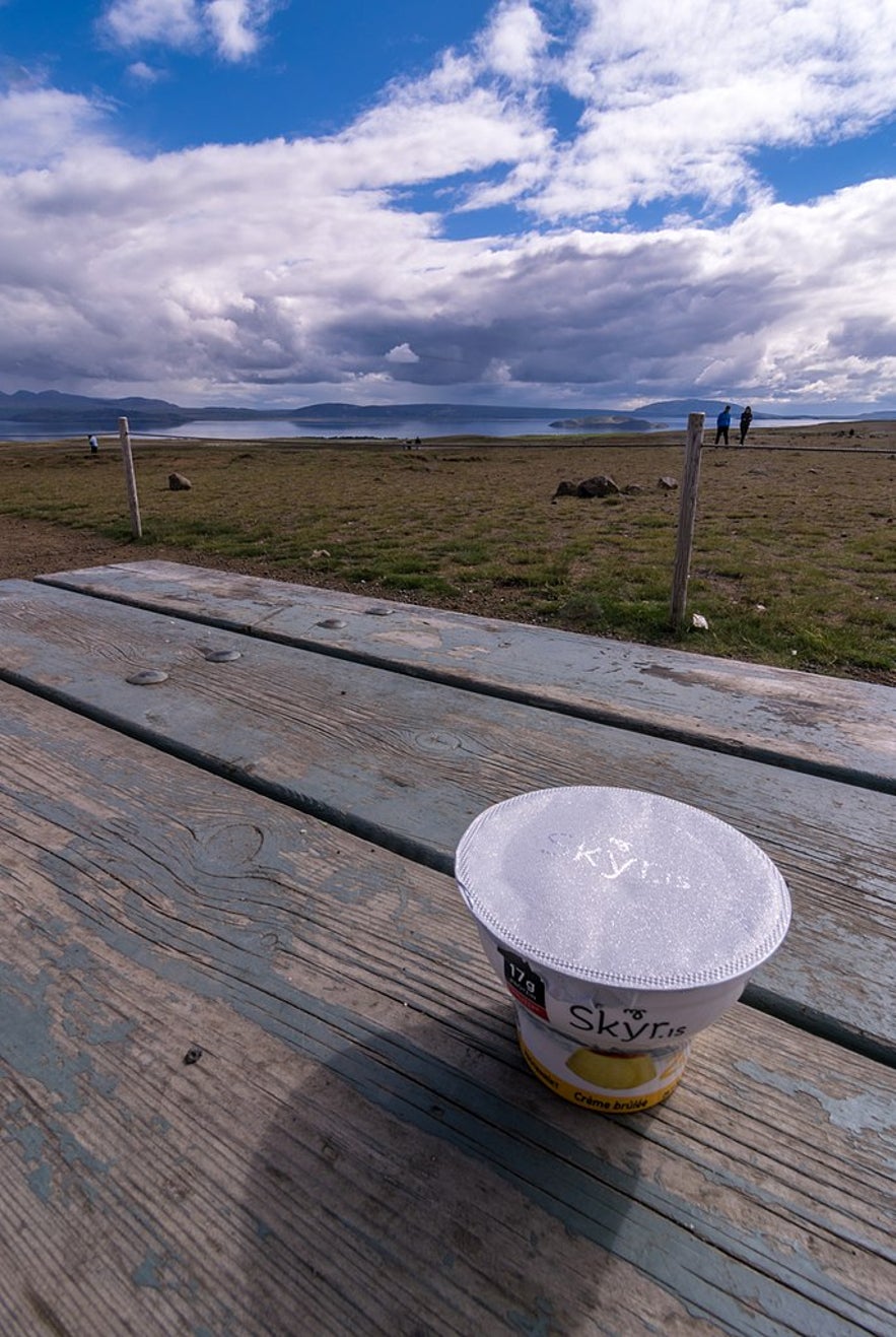 在户外野餐长椅上放着一盆skyr，背景是群山和峡湾。