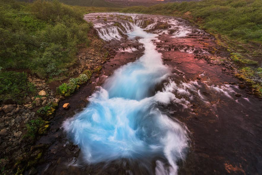 La cascade de Bruarfoss en Islande avec son cours d’eau d’un bleu saisissant traversant un paysage volcanique noir.