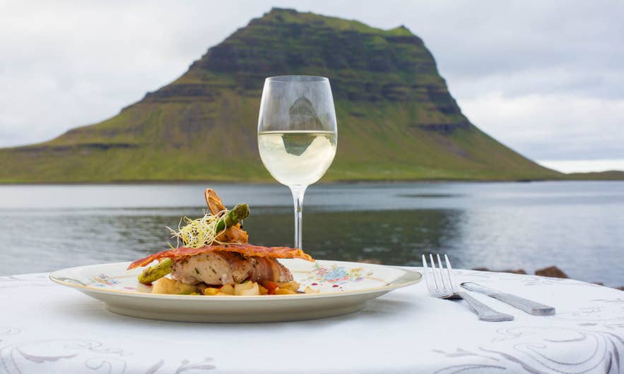 A gourmet dish on a decorated plate sits on a table by a calm lake, with a glass of white wine. A gourmet dish on a decorated plate sits on a table by a calm lake, with a glass of white wine.
