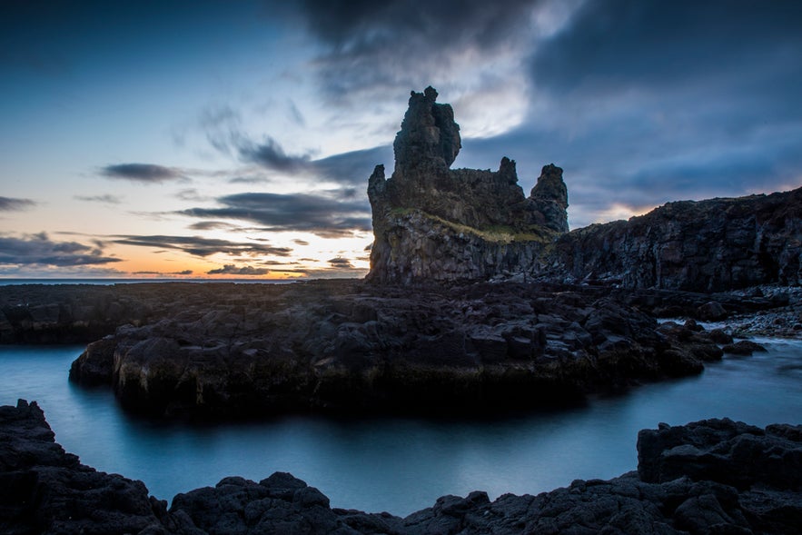 Dramatic sunset over Londrangar cliffs with rugged volcanic rocks and calm coastal waters in West Iceland.