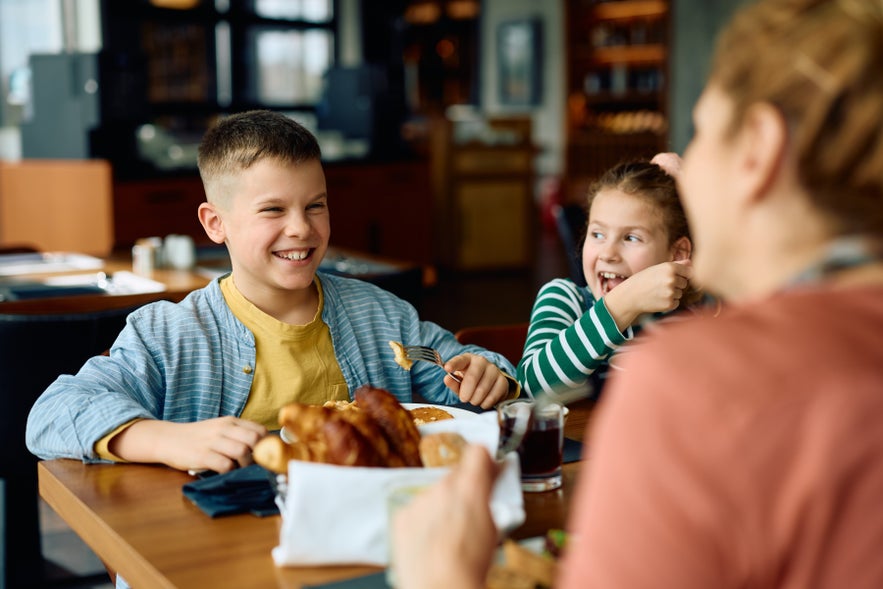 Happy kid eating breakfast and having fun with his family in a restaurant in Reykjavik