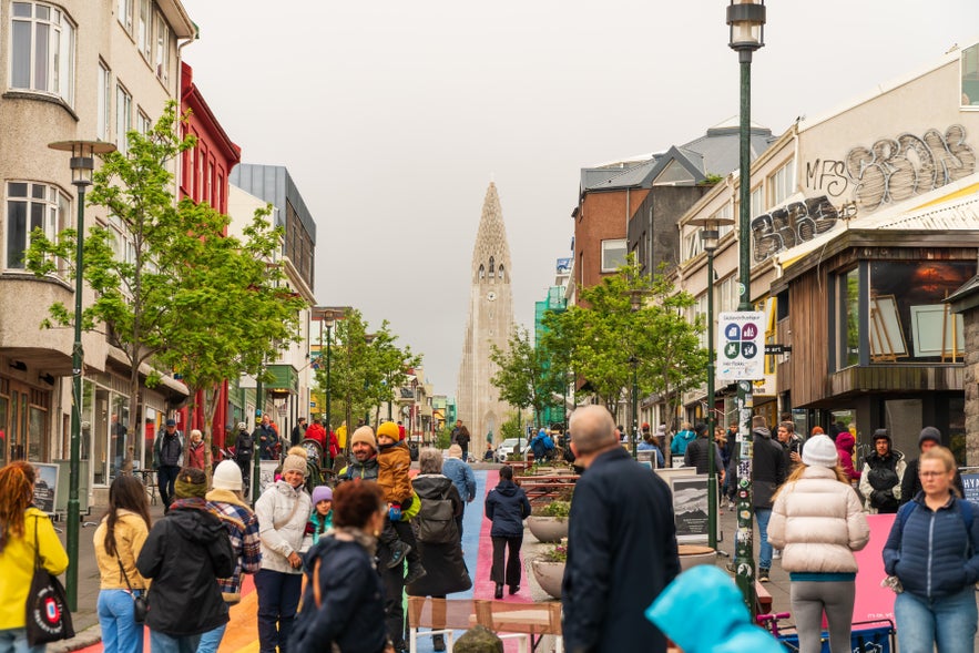 Sk&oacute;lav&ouml;r&eth;ust&iacute;gur street leading up to the Hallgrimskirkja church, tourists posing for photos, people walking, early summer, grey sky.