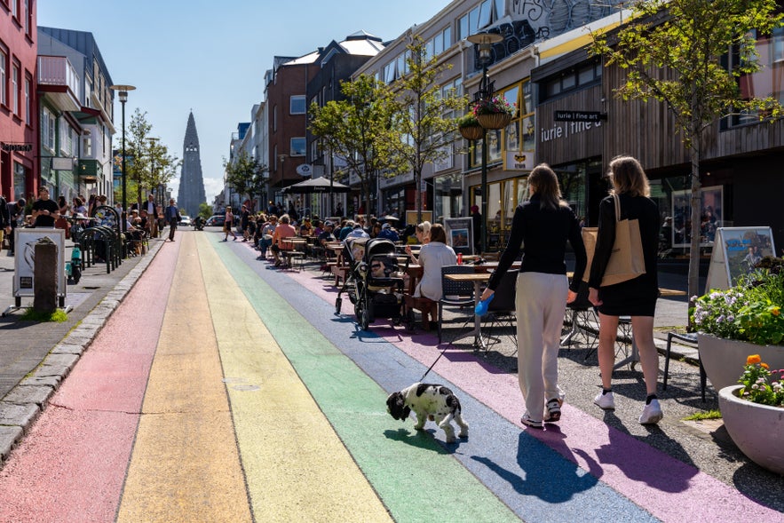 Two women shopping and walk a dog along the famous Rainbow Road in the capital city of Iceland