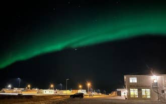Northern lights glow above Adventure Hotel Hellissandur with streetlights and buildings lit under the night sky.