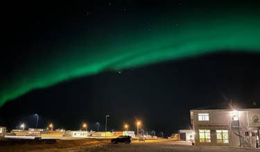 Auroras boreales iluminan el cielo sobre Adventure Hotel Hellissandur, con farolas y edificios encendidos bajo la noche.