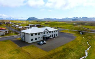 Adventure Hotel Hellissandur sits along a quiet road with mountain views and grassy fields all around.