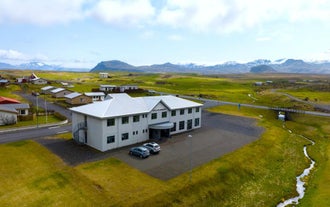 Adventure Hotel Hellissandur sits along a quiet road with mountain views and grassy fields all around.