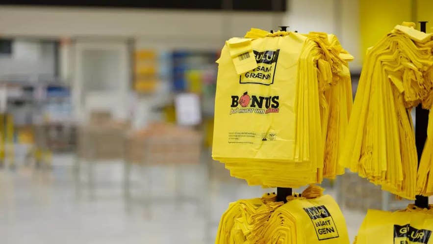 Stapels felgele plastic boodschappentassen met het Bonus-logo en de slogan in een Bonus supermarkt in IJsland.