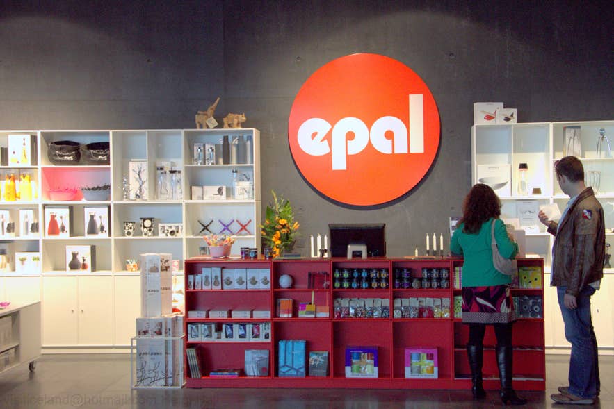 Innenansicht des Epal-Designshops in Reykjavik, Island, mit auffälligem rotem Logo, minimalistischen Regalen mit nordischem Wohnzubehör und Geschenken sowie zwei Kunden, die moderne Dekoartikel durchstöbern.