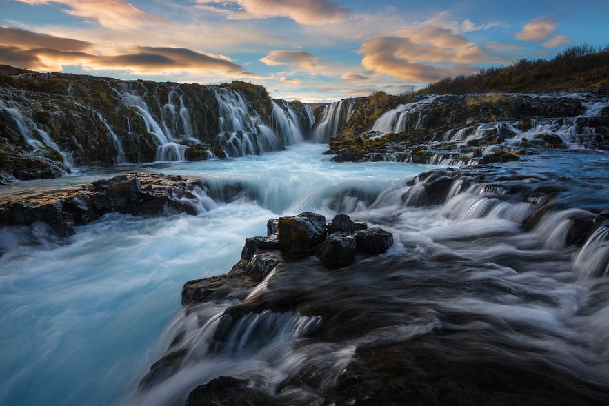 Bruarfoss Waterfall along Iceland's Golden Circle at sunset, featuring blue glacial water cascading over black volcanic rocks.