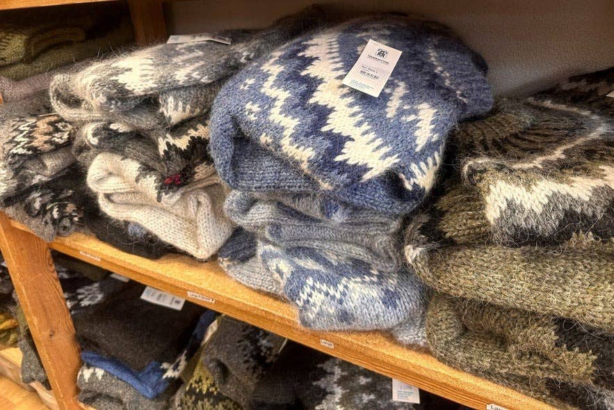 Traditionelle islandske lopapeysa-trøjer i jordfarver og blå nuancer ligger stablet på træhylder i butikken tilhørende Islands Håndstrikkeforening i Reykjavik.