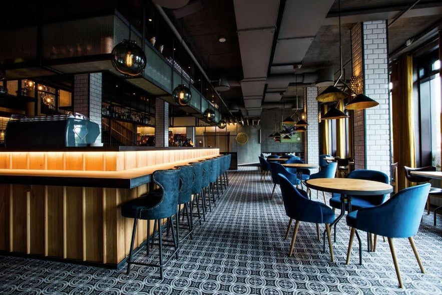 Stylish bar and dining area at Canopy by Hilton Iceland with blue chairs and patterned tile flooring.