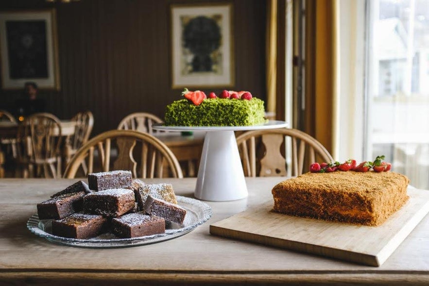 Dessert table at Hotel Aldan in Iceland with brownies, a green pistachio cake, and a honey cake topped with berries.