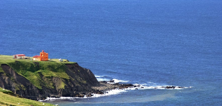 Bright orange Skalatoftanes Lighthouse on a grassy cliff along the Skagi Peninsula in North Iceland, overlooking the Arctic Ocean.