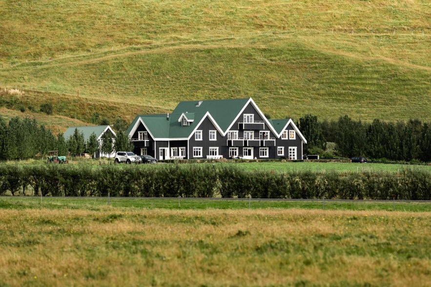 Skalakot Manor Hotel with dark timber walls and green rooftops, set in the grassy hills of southern Iceland.