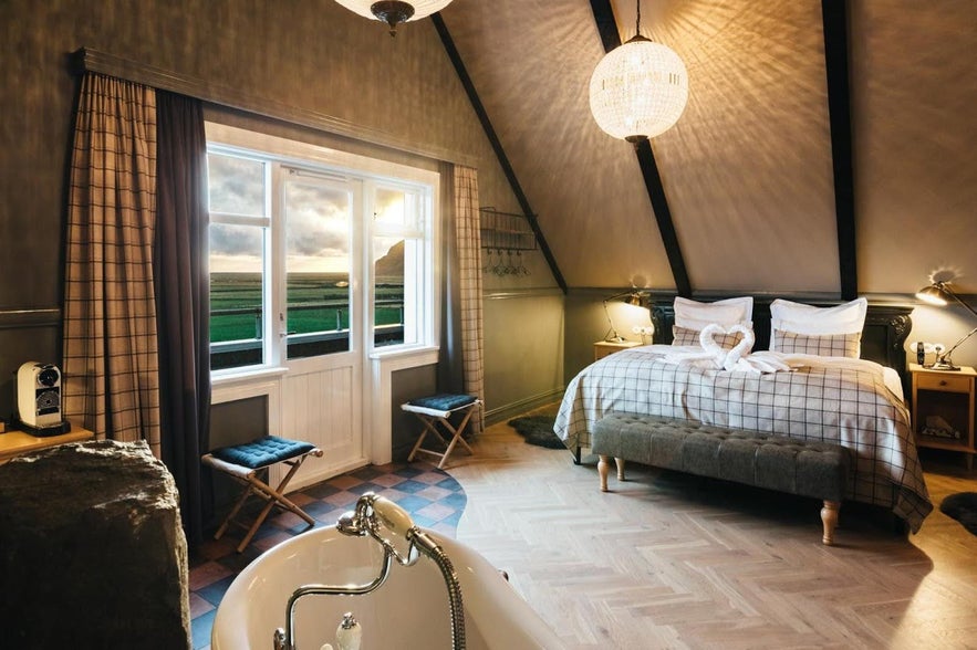 Cozy room at Skalakot Manor Hotel in Iceland with a freestanding tub, plaid bedding, and countryside views.