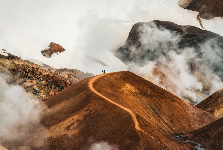 Two hikers walking along a narrow trail in the steaming, colorful rhyolite mountains of Kerlingarfjoll, Iceland.