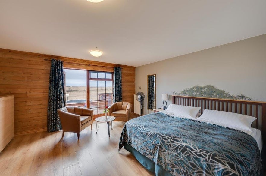 Cozy room at Hotel Ranga in Iceland with a king bed, leather chairs, and countryside views through large windows.