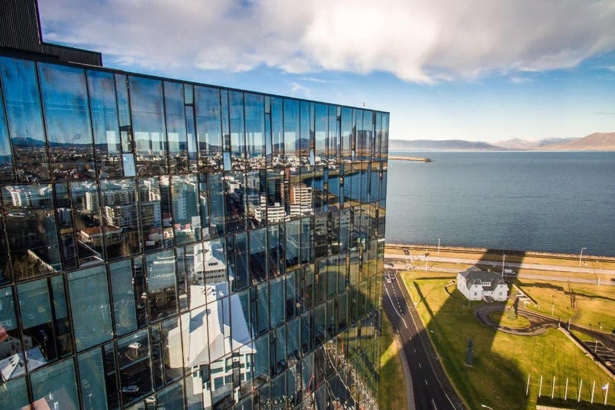 Glass exterior of Tower Suites Reykjavik reflecting the cityscape, with views of the bay and distant mountains.