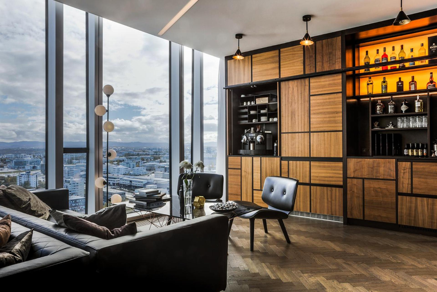 Lounge at Tower Suites Reykjavik with leather chairs, wood-paneled bar, and floor-to-ceiling windows overlooking the city skyline.