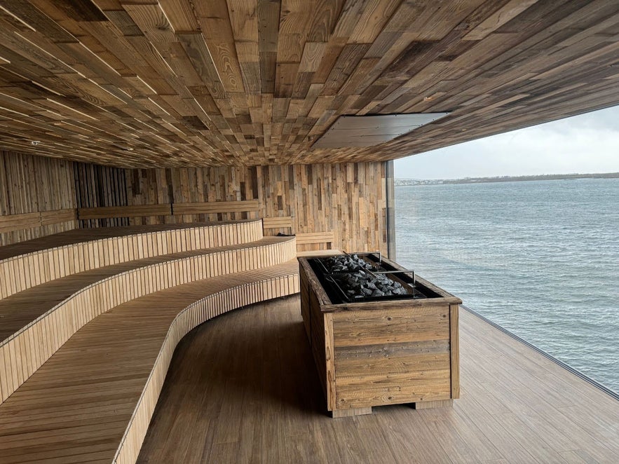 Curved wooden sauna interior at Sky Lagoon in Reykjavik with panoramic ocean views through a large glass wall.