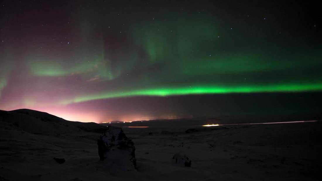 The aurora borealis shining in the sky above a snowy landscape in Iceland.