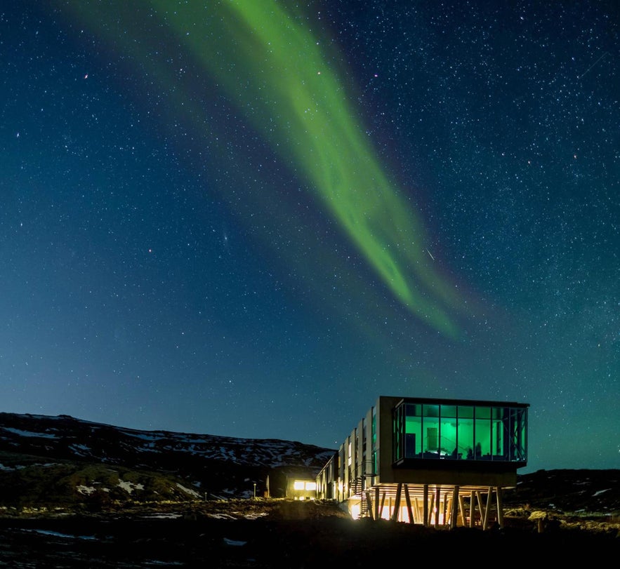 ION Adventure Hotel in Iceland lit up at night with northern lights glowing in the sky above.
