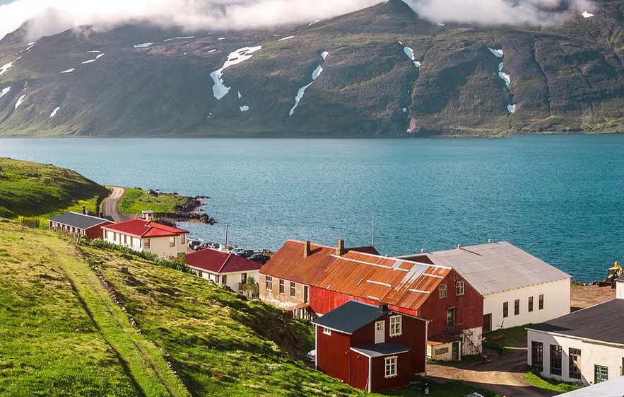 Colorful houses in Seydisfjordur, Iceland, set along a fjord with snow-streaked mountains in the background.