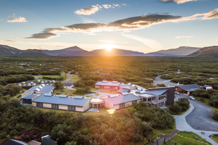 Hotel Husafell in West Iceland surrounded by green hills and mountains, with the sun setting behind the horizon.