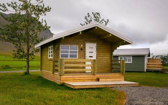 A small rustic cottage with a small terrace outside sits in a grassy field at Moar Cottages in Akranes, West Iceland.