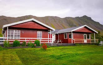 Front view of Moar Guesthouse with red timber siding, picnic table, and a scenic mountain backdrop in West Iceland.