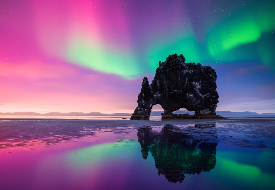 Hvitserkur sea stack reflected in water under vibrant northern lights in North Iceland.