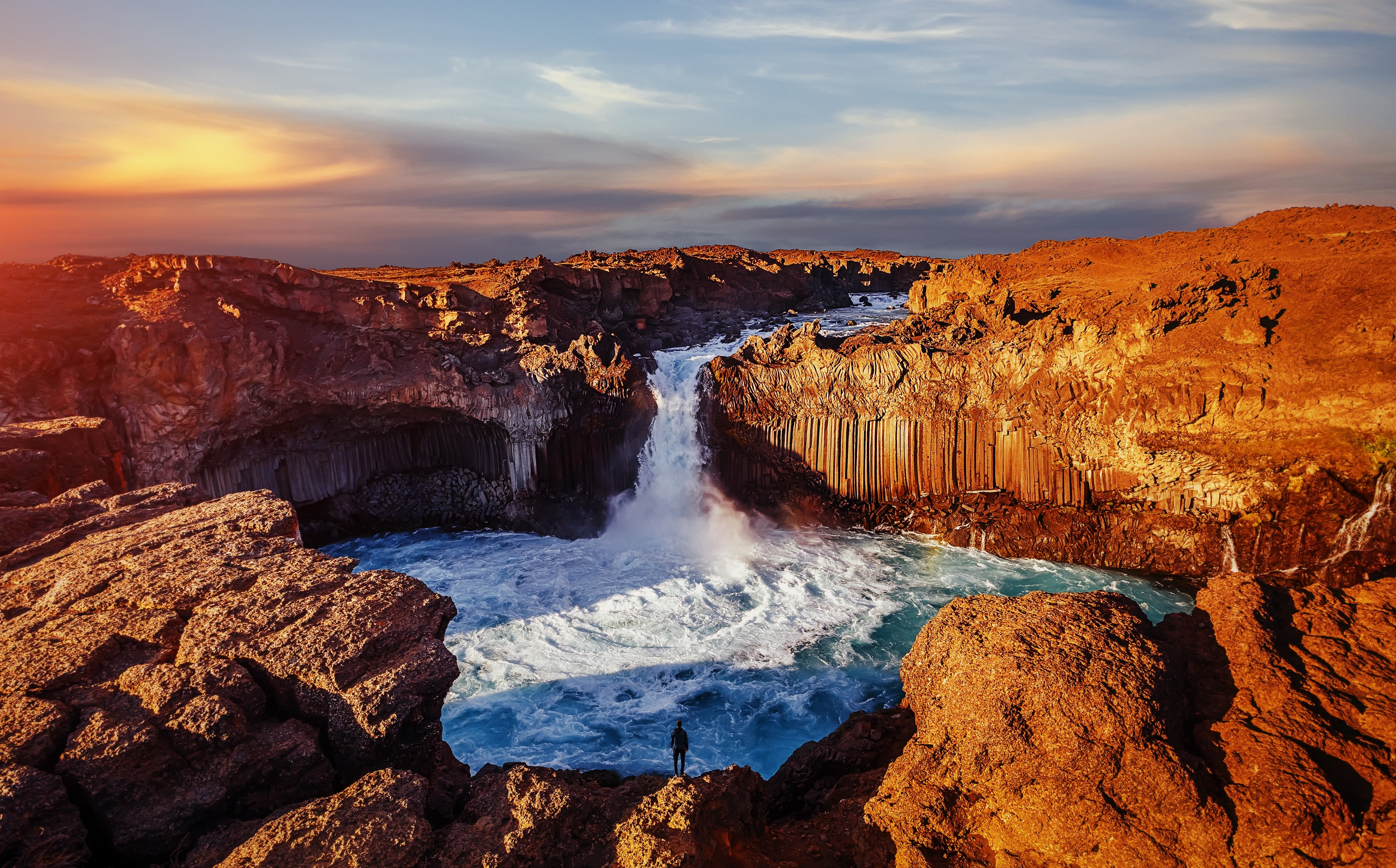Aldeyjarfoss waterfall cascading between basalt columns into a blue pool at sunset in North Iceland.