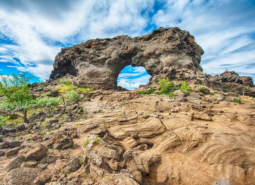 Lava arch formation surrounded by volcanic rock and greenery in Dimmuborgir, North Iceland.