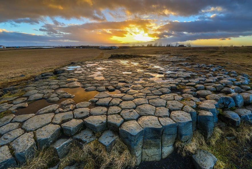 Hexagonal basalt tiles of Kirkjugolf reflecting golden sunset light in South Iceland.