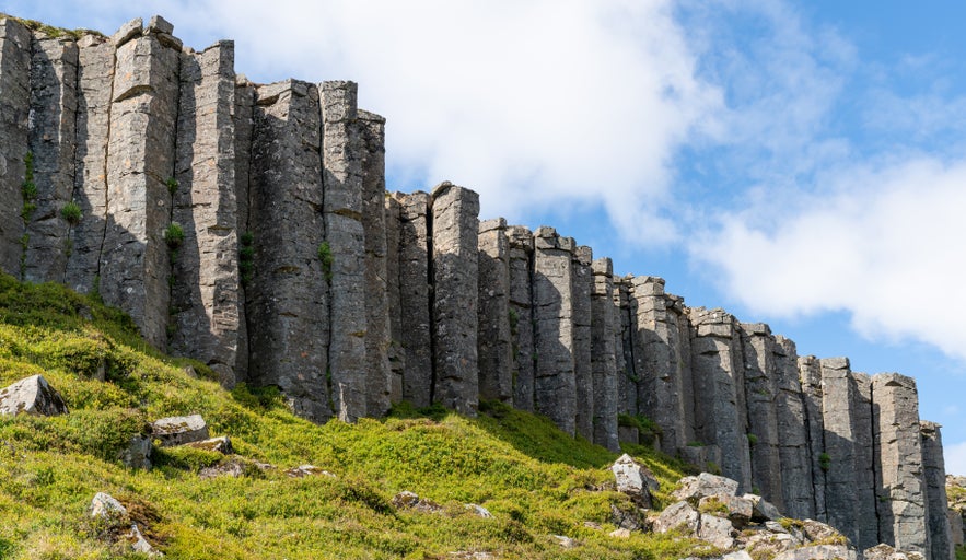 Tall, evenly spaced basalt columns of Gerduberg rising above grassy slopes in West Iceland.