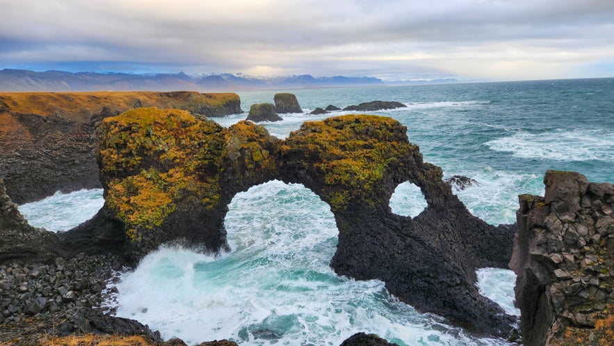 Sea arch of Gatklettur with waves crashing below and moss-covered lava rock on the Snaefellsnes Peninsula, Iceland.