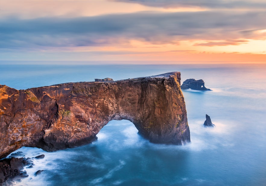 Natural sea arch of Dyrholaey rising above calm ocean waters at sunset in South Iceland.