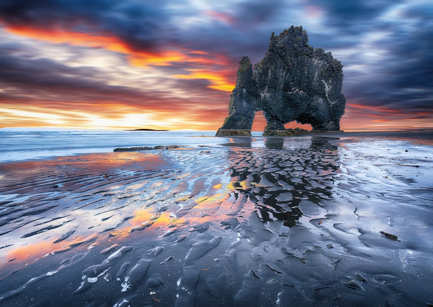 Hvitserkur sea stack reflected on wet sand at low tide during a vivid sunset in North Iceland.