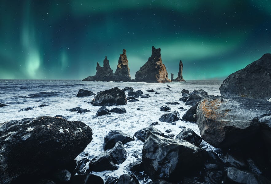  Reynisdrangar sea stacks rising from the ocean under the Northern Lights near Vik, Iceland.