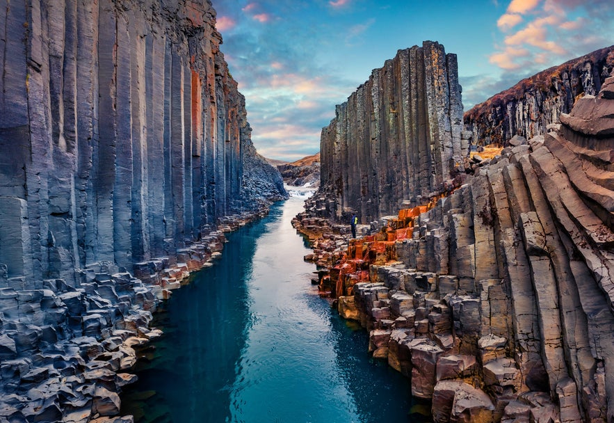 Basalt column walls rising along a turquoise river at sunset in Studlagil Canyon, East Iceland.