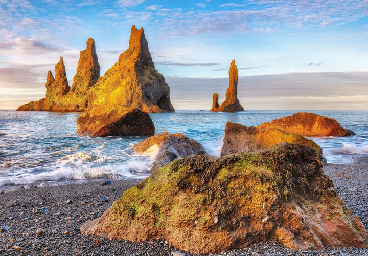Reynisdrangar sea stacks glowing in sunset light off the black pebble beach near Vik, Iceland.