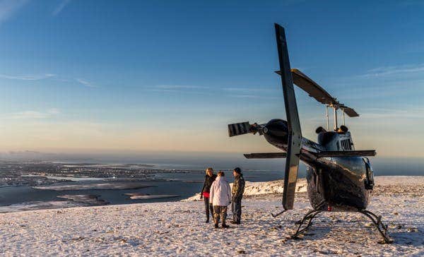 During a summit landing, people get out of the helicopter and enjoy marvelous views of the mountains, villages, ocean, and islands near Reykjavik.