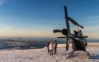 During a summit landing, people get out of the helicopter and enjoy marvelous views of the mountains, villages, ocean, and islands near Reykjavik.