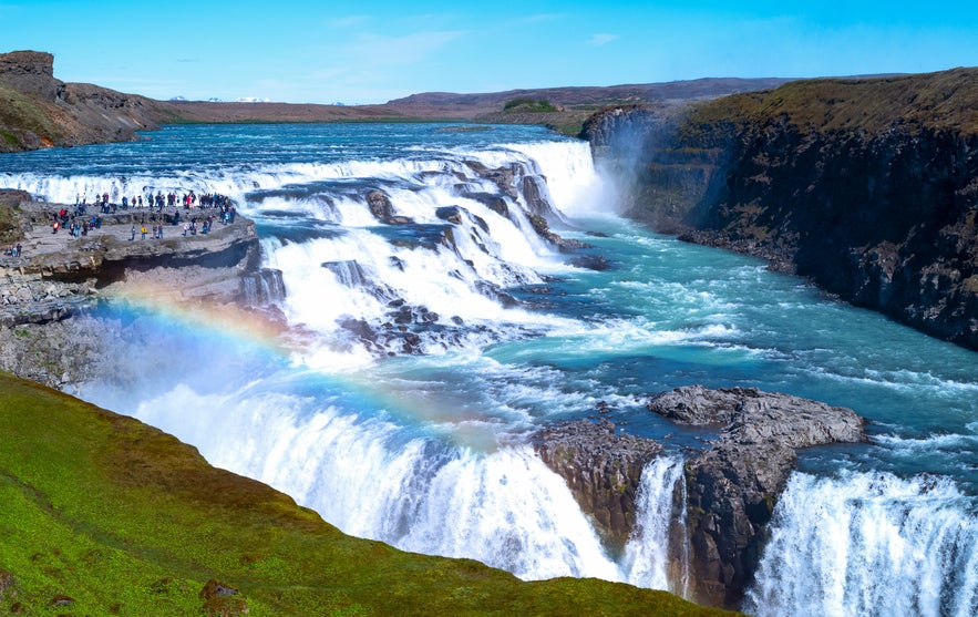 Gullfoss waterfall with rainbow and tourists at viewing platform in South Iceland.