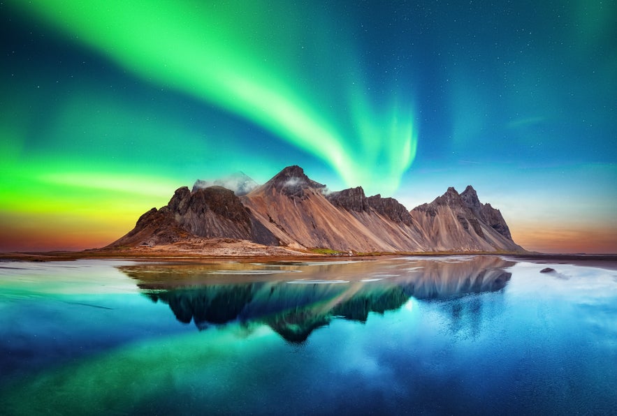 Northern lights over Vestrahorn mountain with lagoon reflections in South Iceland.