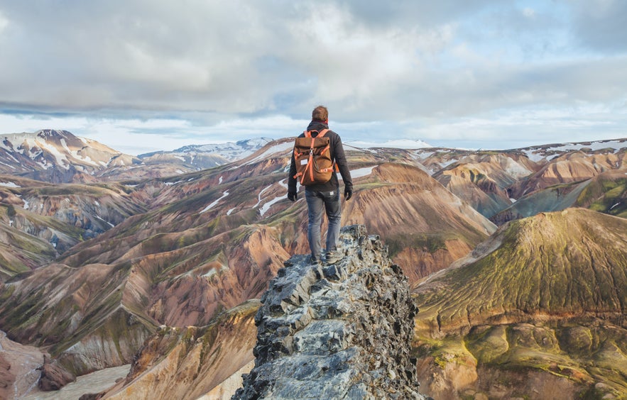 Hiker standing on a rocky peak overlooking colorful rhyolite mountains in Landmannalaugar, Iceland Highlands.